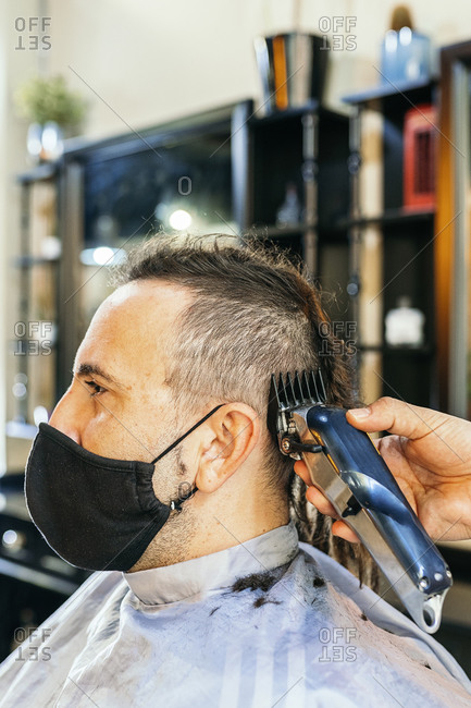 Unrecognizable crop male hairdresser using trimmer and grooming hair of man with dreadlocks in contemporary barbershop