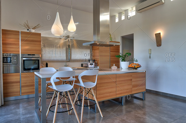 Interior of modern kitchen in apartment with wooden dining table and glowing lamps hanging from ceiling