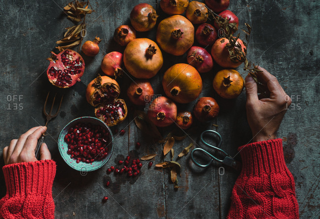 From above unrecognizable hand of person standing at rustic table and putting on ripe fresh pomegranates in pile in dark room