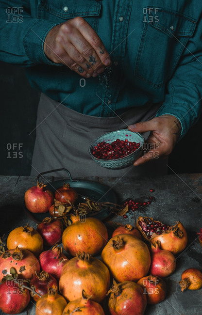 High angle of male cook sprinkling sugar in bowl with delicious ripe pomegranate seeds while standing at rustic table