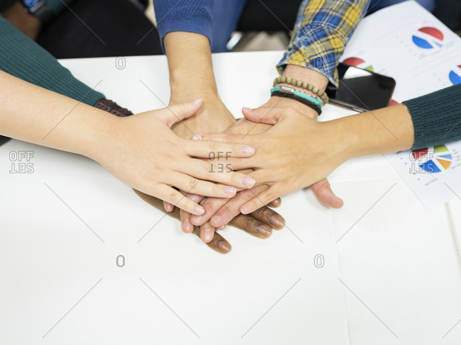 From above of crop anonymous multiracial colleagues in casual clothes gathering around table with charts and stacking hands together while working on business development plan in workplace