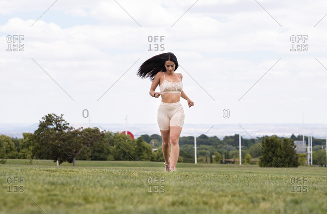 Full body of young fit female in trendy activewear running on green grassy meadow towards camera during fitness training in park