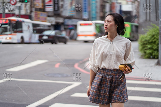 Calm Asian female in casual style clothes walking along crosswalk and looking away in Taichung city