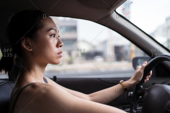 Side view of focused Asian female driving modern automobile along road in Taichung city