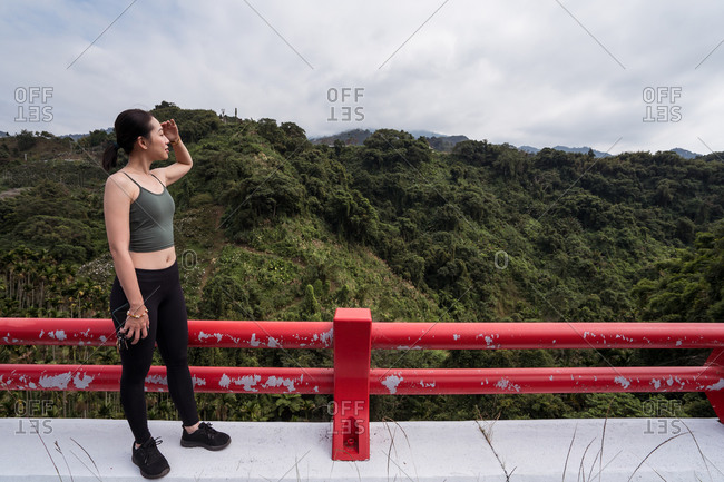 Side view of ethnic female traveler standing at viewpoint and admiring amazing scenery of green highland terrain in Taichung