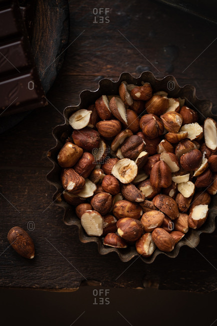 Top view of nutritious hazelnuts placed in metal bowl on wooden table in dark kitchen