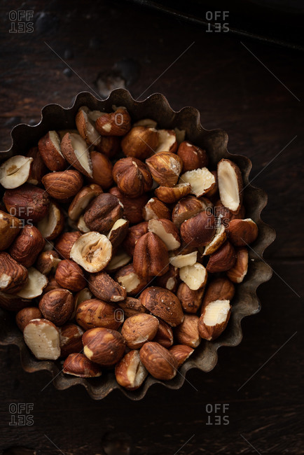 Top view of nutritious hazelnuts placed in metal bowl on wooden table in dark kitchen