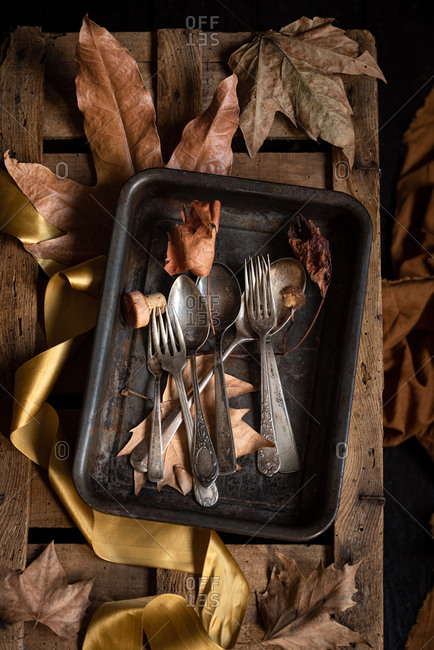 Top view of retro metal spoons and forks placed on rustic wooden palette with dried autumn leaves
