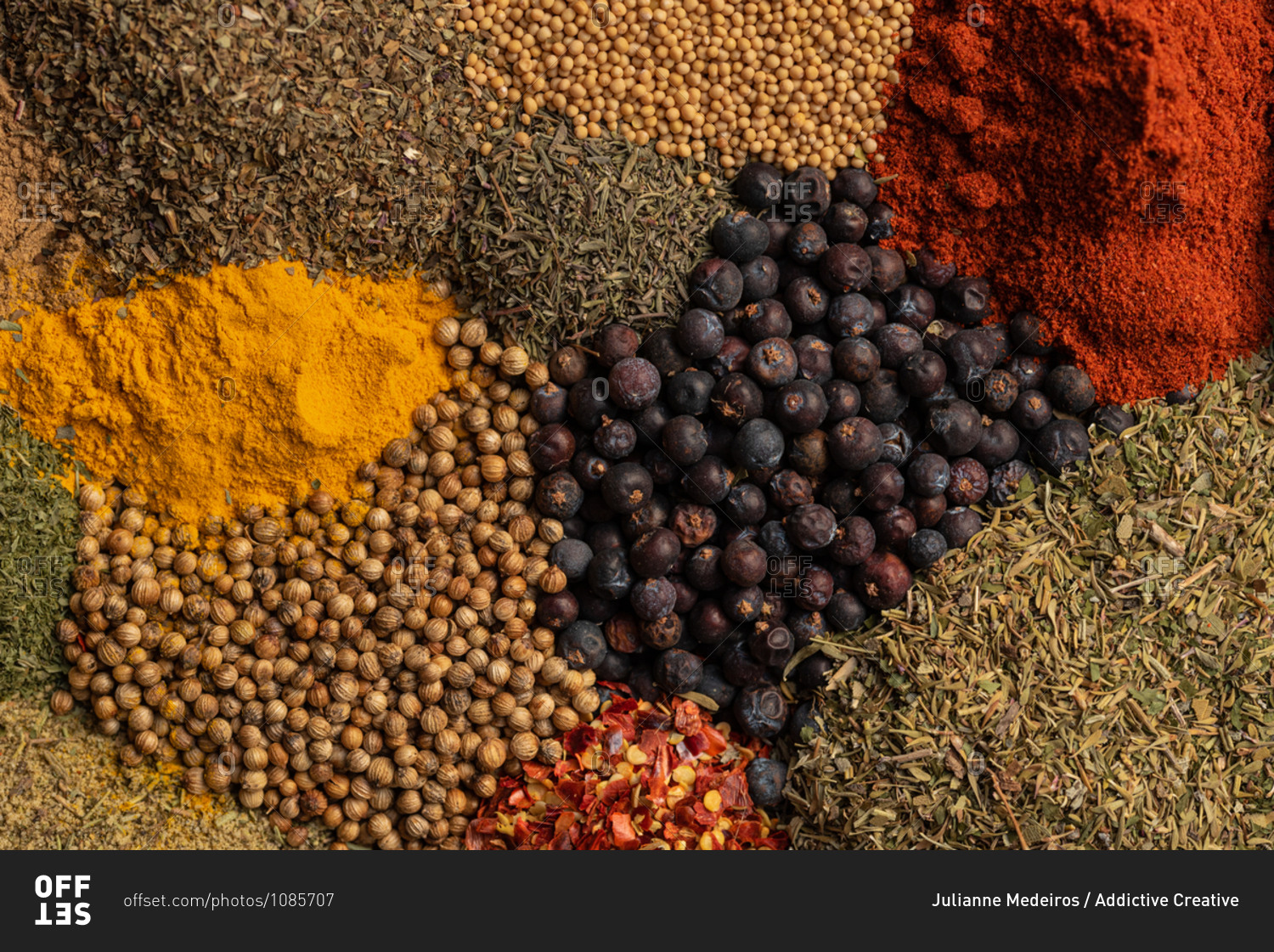 Top view closeup of pile of assorted aromatic dried spices including various types of pepper and herbs with paprika and turmeric powder scattered together