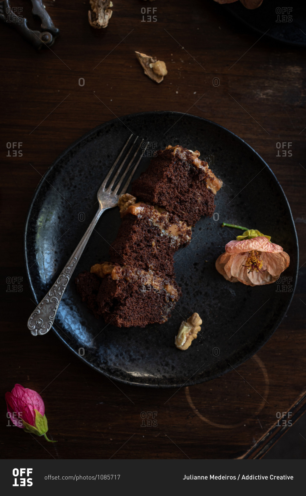 Top view of pieces of delectable layered chocolate cake with walnuts served on black plate with fork and garnished with flower buds