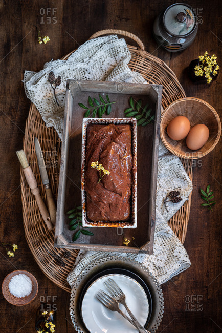 Top view composition with palatable homemade rustic chocolate pound cake in baking dish placed on wooden table with ingredients and cuttlery
