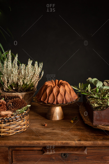 Delicious homemade bundt cake placed on rustic wooden table near wicker basket with flowers