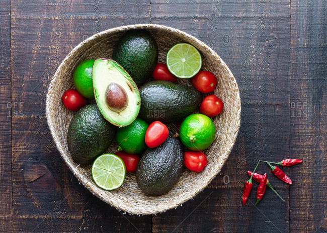 Top view bowl with fresh avocado and lime with tomatoes placed on wooden table with spices for traditional Mexican guacamole recipe