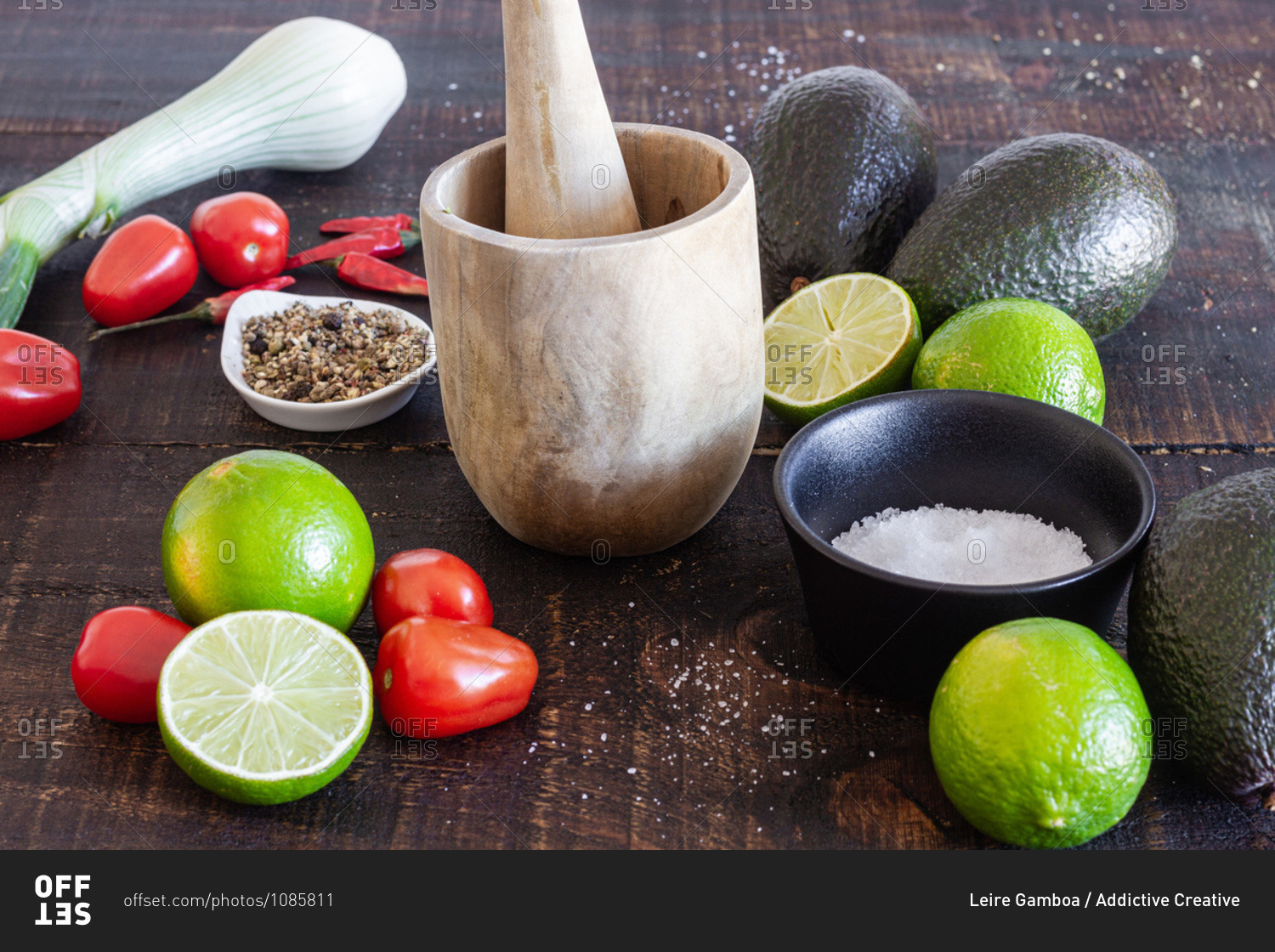 Fresh avocado and lime with tomatoes placed on wooden table with green onion and spices for traditional Mexican guacamole recipe