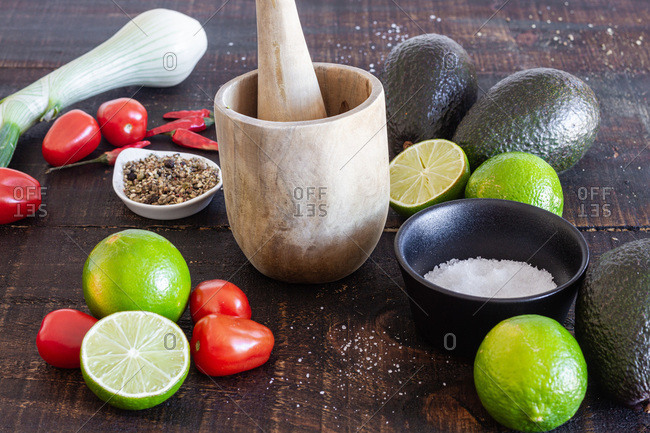 Fresh avocado and lime with tomatoes placed on wooden table with green onion and spices for traditional Mexican guacamole recipe
