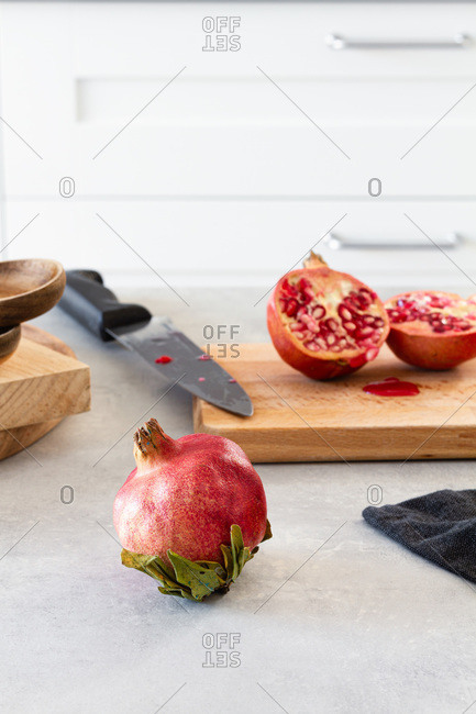 Whole and halved fresh ripe juicy pomegranate on kitchen table with cutting board and knife