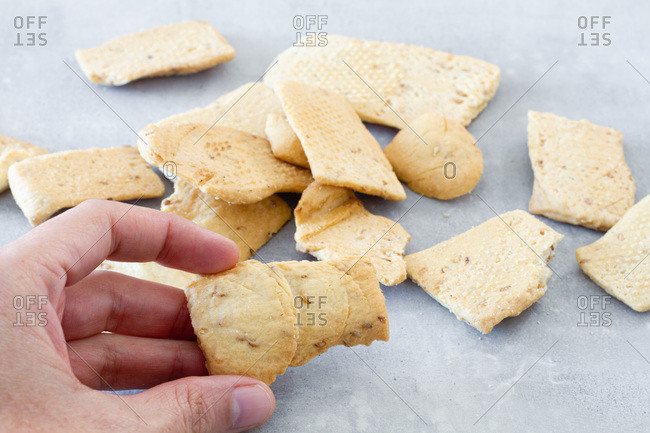 Closeup of crop anonymous person taking crispy salted cracker from table while preparing food in kitchen