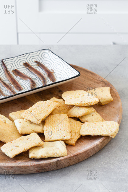 Heap of crispy salt crackers served on wooden board near plate with canned fish as appetizer