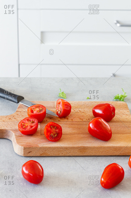 Wooden cutting board with cut juicy cherry tomatoes prepared for Caesar salad on counter