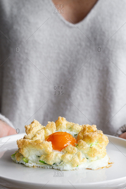Crop anonymous housewife holding plate with appetizing freshly made cloud eggs with green vegetables served with crackers for healthy breakfast