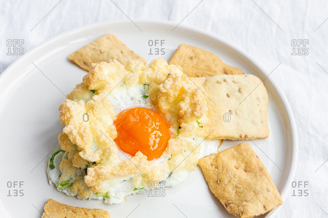High angle of appetizing homemade baked cloud eggs with green vegetables served with crispy crackers for healthy breakfast