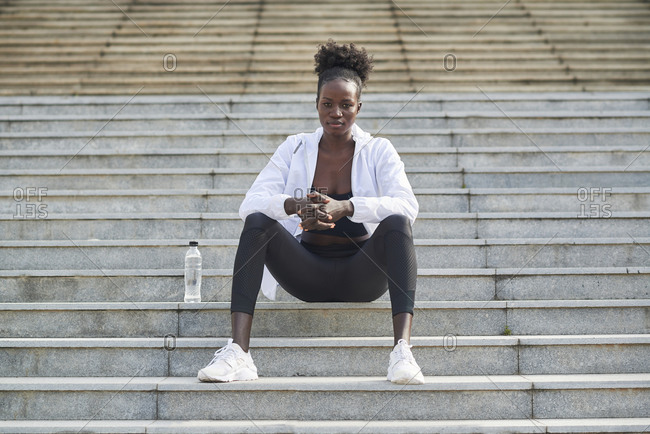 Relaxed African American female runner sitting on stairs in city relaxing after during training looking at camera