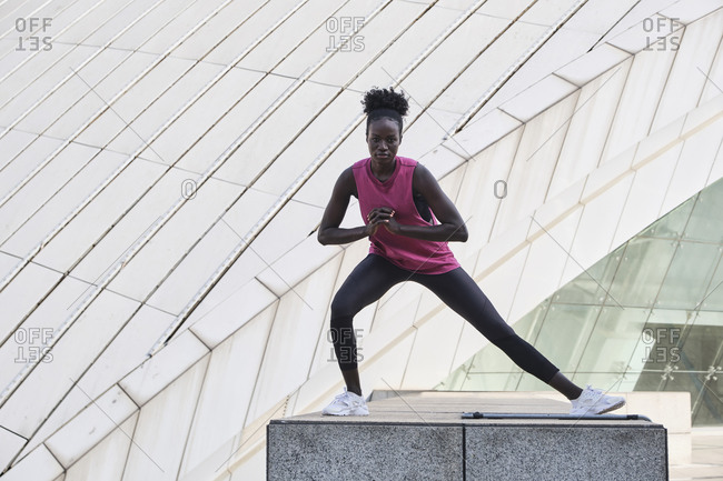 Determined African American female athlete in activewear doing side lunges and stretching legs during training on street while looking at camera