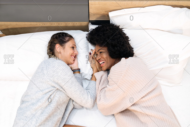 From above of delighted young multiracial lesbian couple in casual clothes lying on bed and enjoying free time together during weekend at home