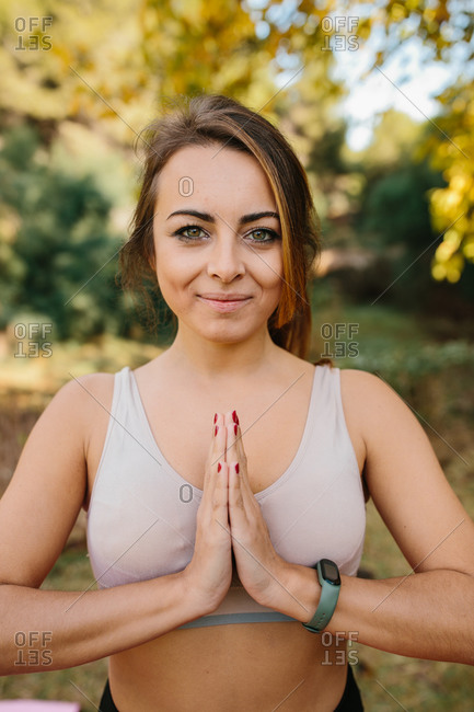 Content female in sportwear practicing yoga in park and standing with Namaste hands while looking at camera