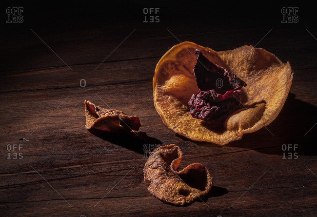 Still life chiaroscuro composition with dehydrated sliced sweet potato and beet arranged in shape of flower on wooden surface
