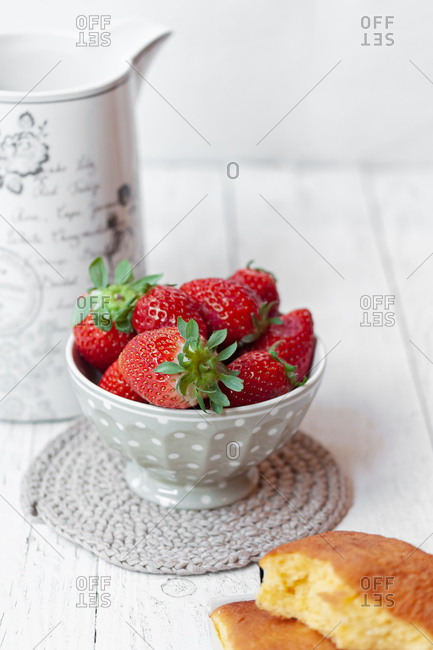 Traditional Spanish sweet sobao cake placed near bowl with fresh ripe strawberries served for delicious breakfast on white wooden table