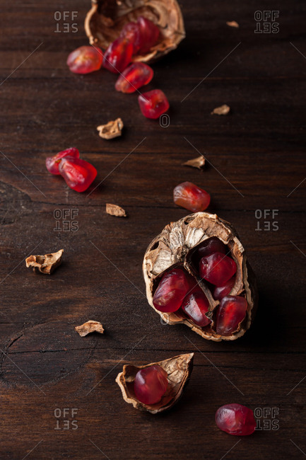 Top view still life composition with ripe red pomegranate seeds arranged in walnut shells on dark wooden background