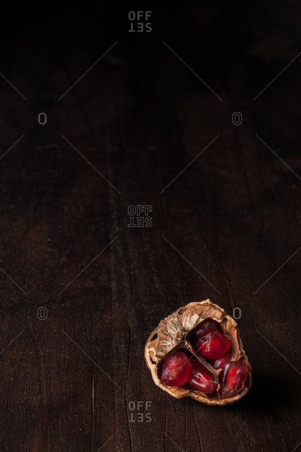 Top view still life composition with ripe red pomegranate seeds arranged in walnut shells on dark wooden background