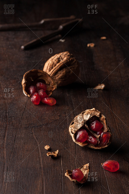 Still life composition with ripe red pomegranate seeds arranged in walnut shells on dark wooden background