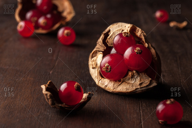 Still life composition with ripe red pomegranate seeds arranged in walnut shells on dark wooden background