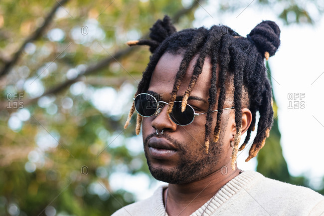 African American man with dreadlocks in bun wearing nose piercing with sunglasses on blurred street background