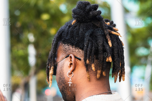 Back view of African American man with dreadlocks in bun wearing ankh earring with sunglasses on blurred street background