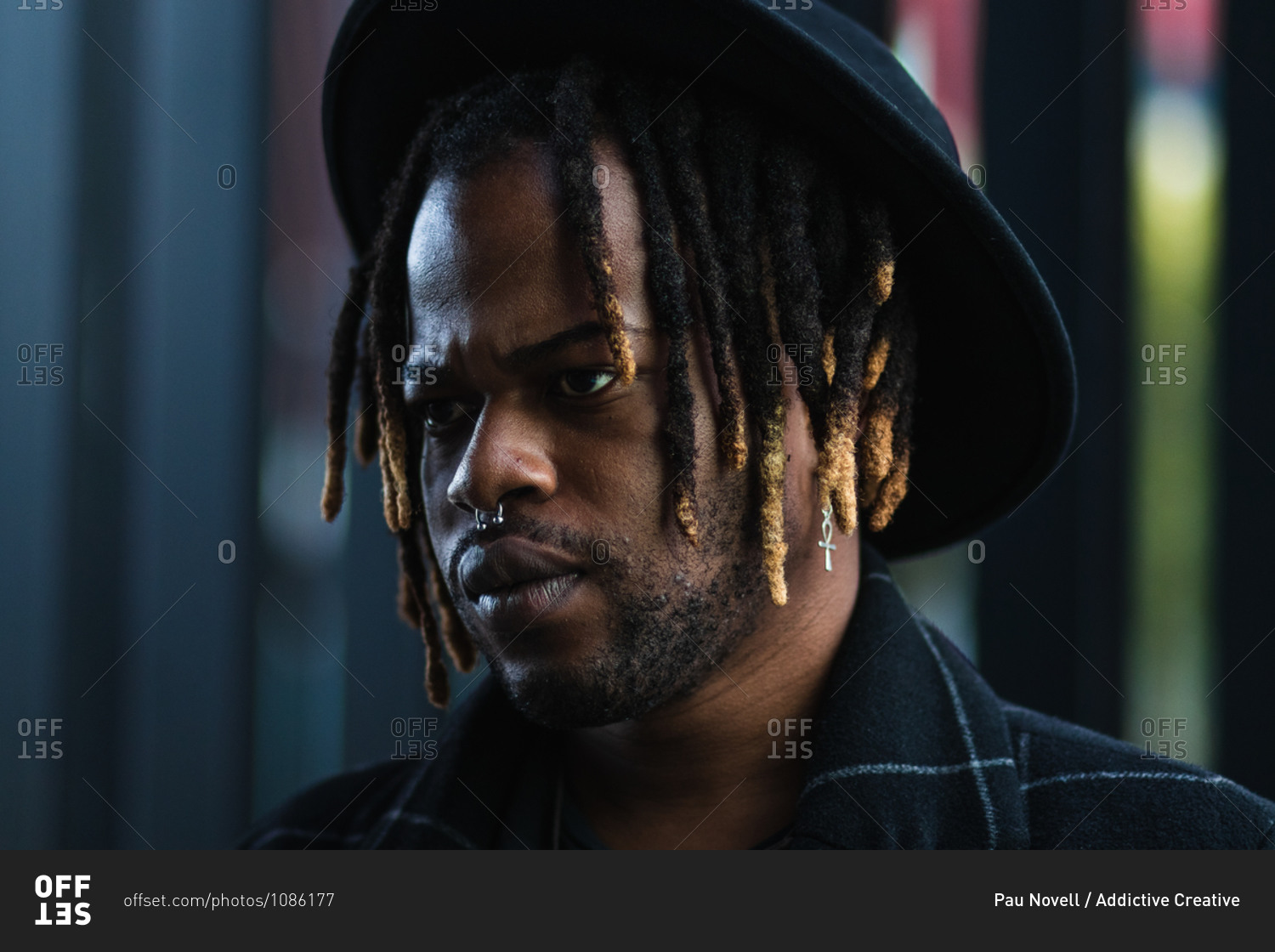 Informal bearded ethnic man with dreadlocks and in hat looking away standing on street