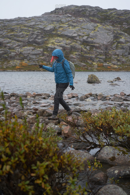 Side view of female explorer in warm clothes crossing river while walking along wet stones in highland area during travel in autumn