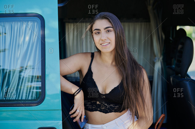Cheerful female wearing summer top sitting in parked van and looking at camera during summer trip