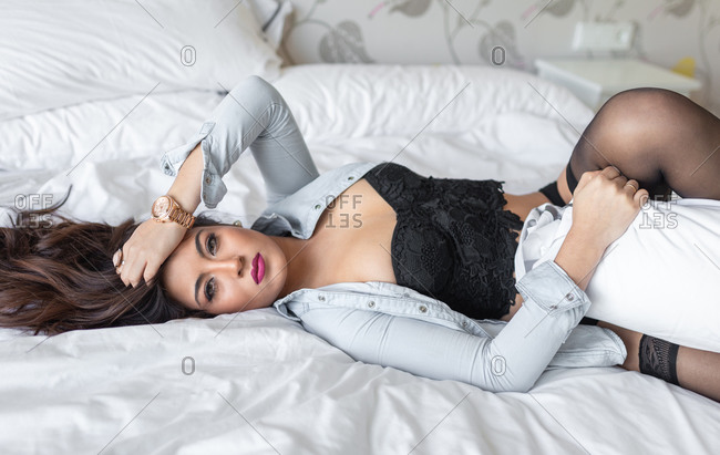 Sexy female in black underwear and shirt lying on soft bed and seductively  looking at camera stock photo - OFFSET