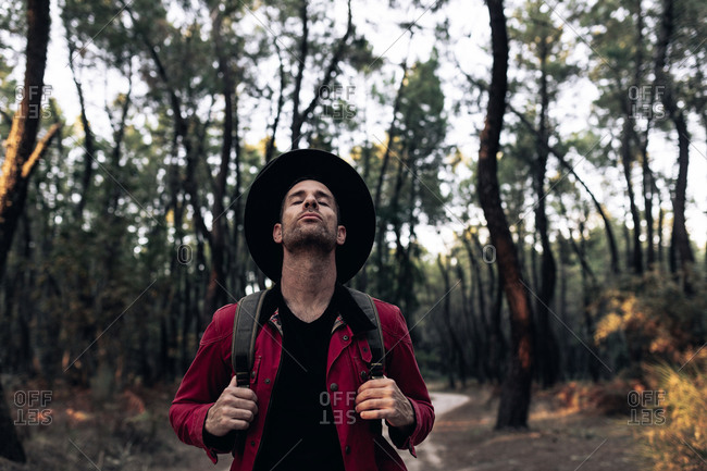 Adult traveler in hat closing eyes and breathing peacefully in harmony with nature of forest