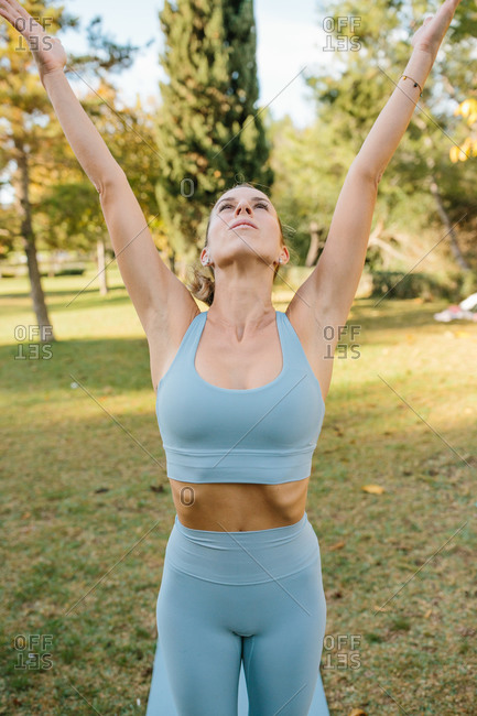 Full body of young slim barefoot female in blue sportswear standing in Crescent Lunge on the Knee pose while practicing yoga on green lawn in park