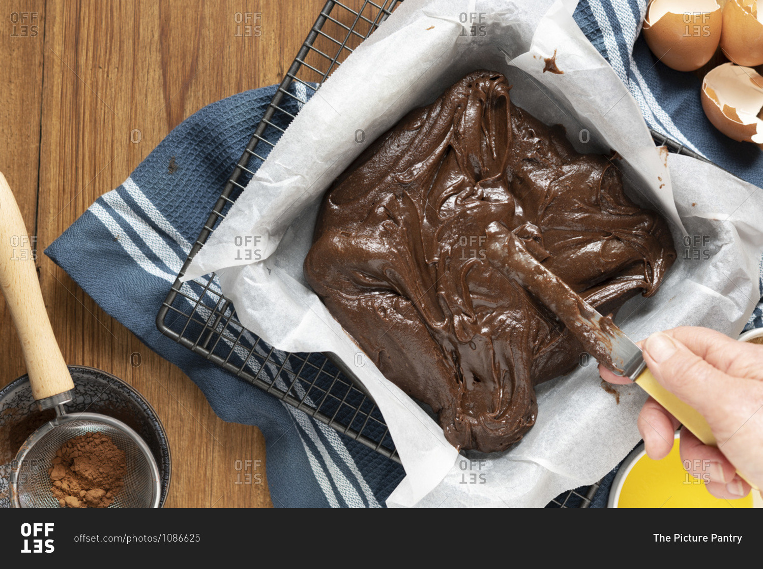 Chocolate cake batter spread into a baking pan with a knife.