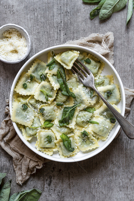 Herb ravioli with butter sage served with a bowl of parmesan cheese