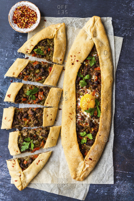 Turkish pide stuffed with beef and an egg photographed on a piece of baking paper on a dark background.