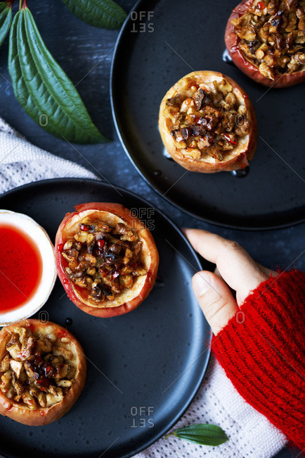 Apples stuffed with walnuts and drizzled with beetroot syrup on two black plates, a woman wearing red sweater holding it.