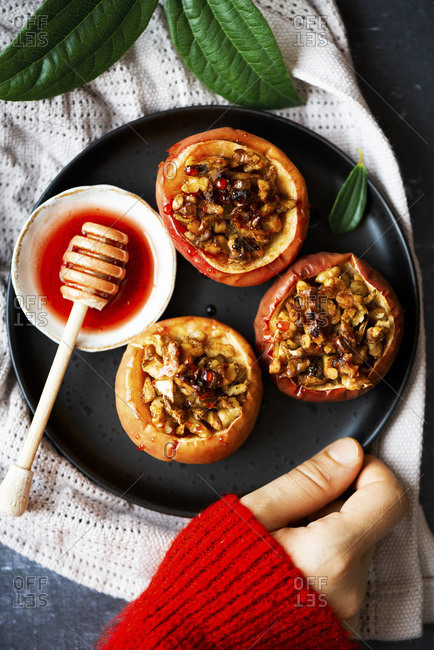Apples stuffed with walnuts and drizzled with beetroot syrup on a black plate, a woman wearing red sweater holding it.