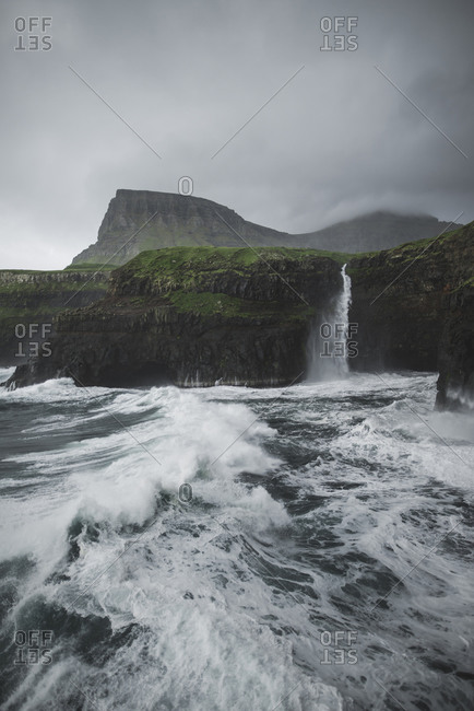 Denmark, Faroe Islands, Gasadalur Village, Mt. Lafossur Waterfall, Coastline with Mulafossur Waterfall falling into Atlantic Ocean in stormy day