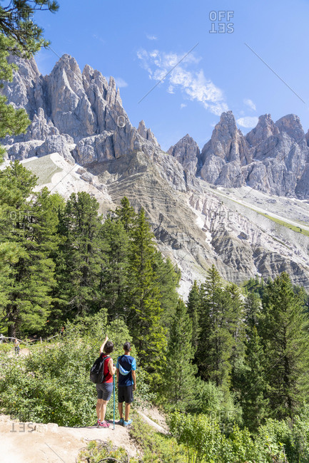 Rear view of two young hikers admiring the Odle from the famous Adolf Munkel trail, Val di Funes, South Tyrol, Dolomites, Italy, Europe